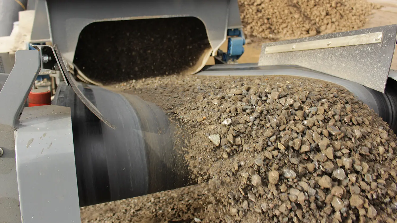 Fresh-crushed basalt aggregate cascading off the discharge conveyor of an RM 100X tracked impact crusher.