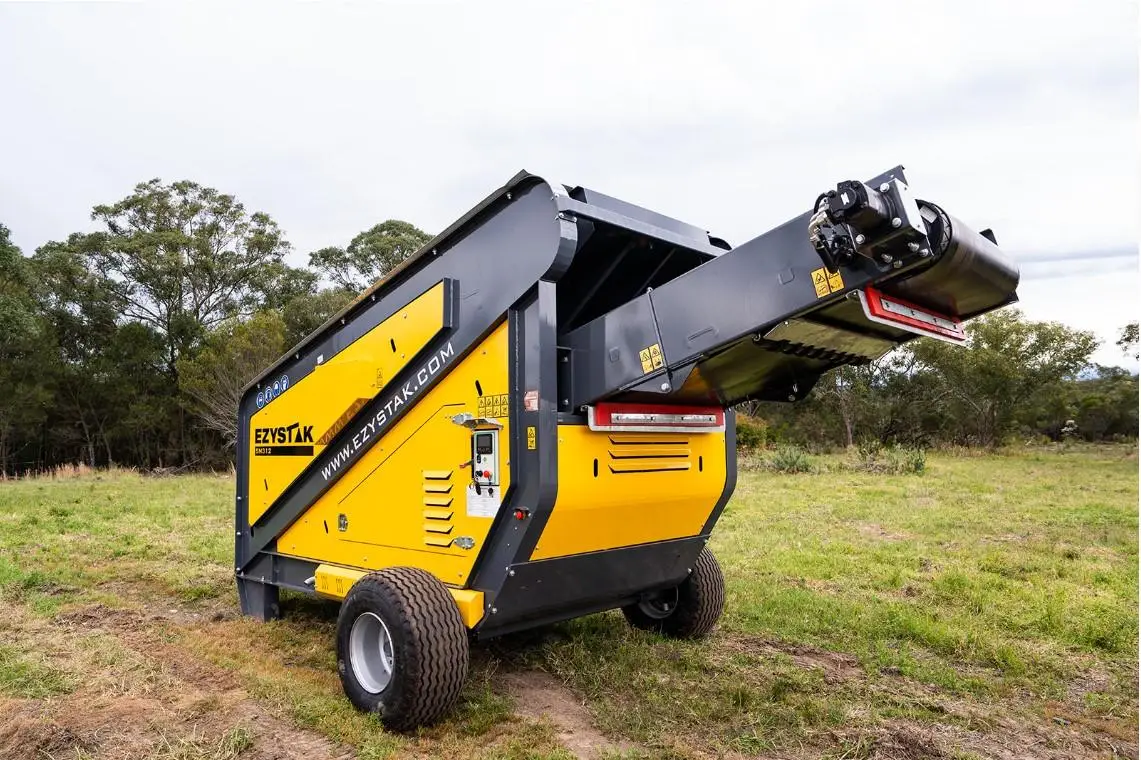 Mobile screener grading crushed rock into separated stockpiles on a quarry floor.