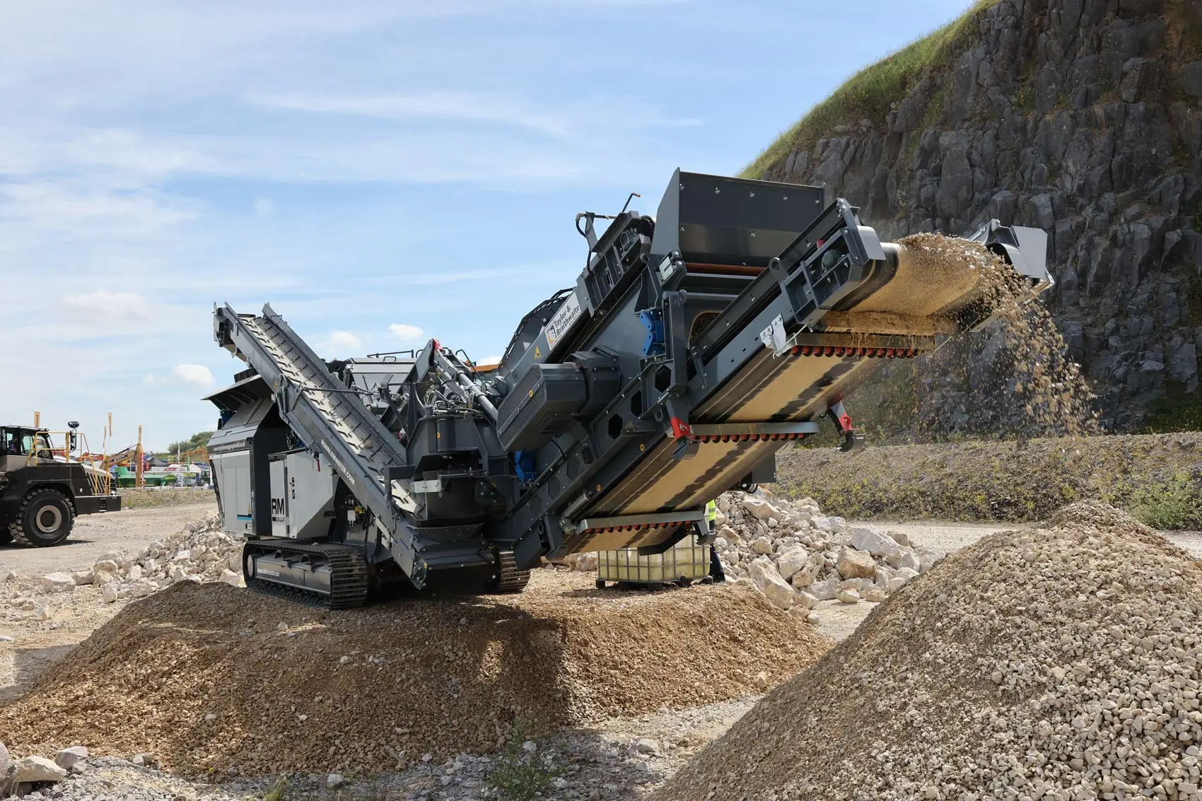 Tracked mobile shredder processing demolition waste with a tall discharge conveyor at an Australian site.
